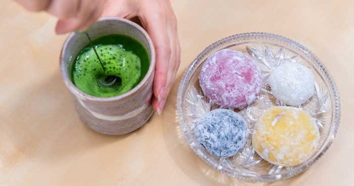 matcha being whisk without a bamboo whisk and wagashi on the side